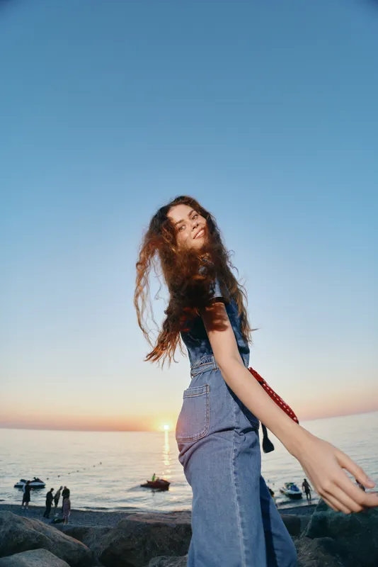 smiling woman in denim outfit enjoying sunset by the sea with relaxed mood and natural light at the beach shore