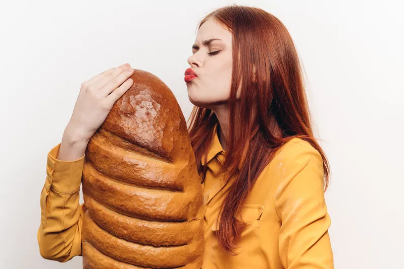 Женщина целует батон на светлом фоне, жёлтая рубашка, мучной продукт, обрезанный вид