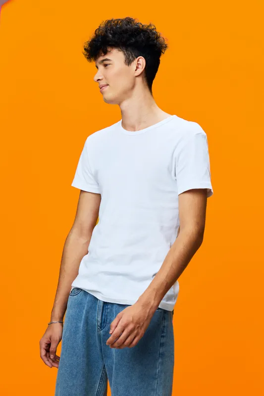 young man wearing casual white t-shirt and blue jeans posing relaxed against bright orange background, curly hair, studio portrait with vibrant colors