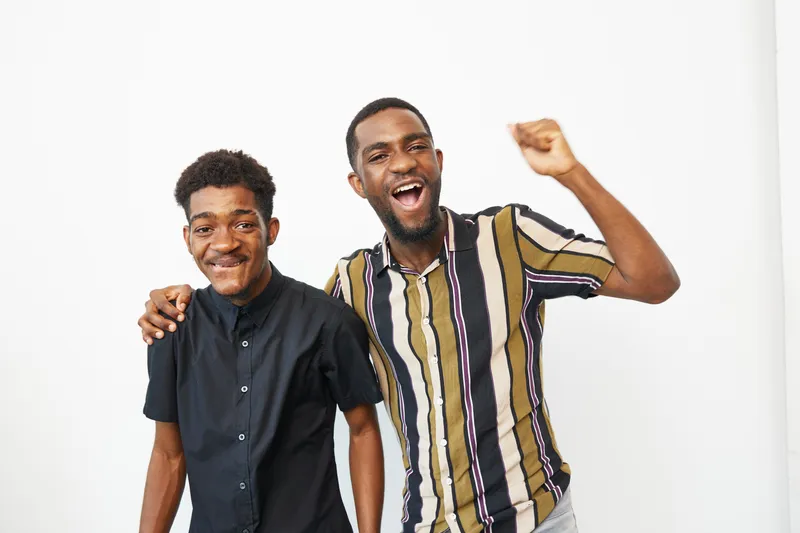 Joyful African American men celebrating together, showcasing their happiness and camaraderie. The vibrant colors of their clothing add to the cheerful atmosphere.