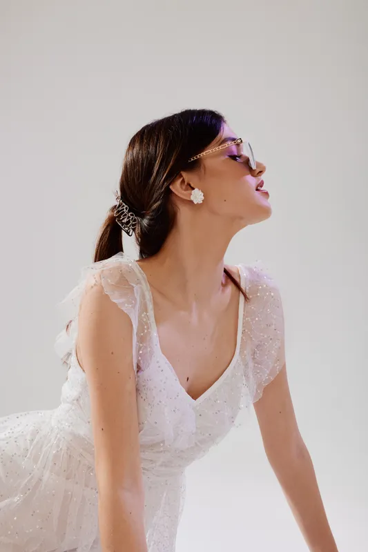Elegant woman in a white lace dress poses with closed eyes and head tilted back. Soft lighting highlights her delicate jewelry and smooth skin. Concept of beauty fashion.