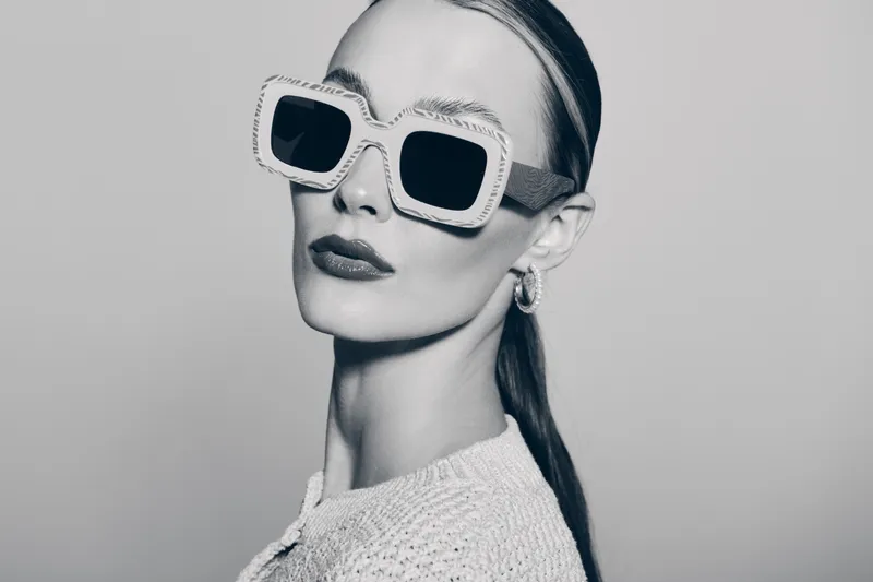 Elegant white woman with fair skin wears large square sunglasses and hoop earrings. Studio portrait with high fashion style and confident look.