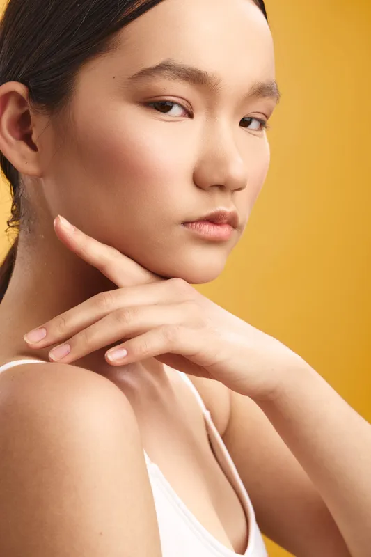 Asian woman appears in a studio portrait, calm and confident, with soft lighting and natural makeup that highlight her poised expression and contemporary style, suggesting focus and professional