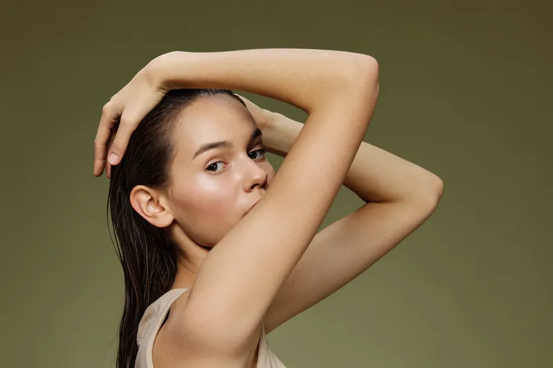 Elegant young woman with wet hair posing against a soft green background, showcasing natural beauty, confidence, and serenity in a minimalist style