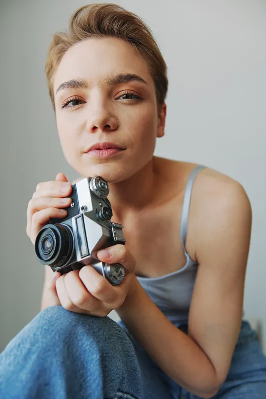 Женщина-фотограф снимает в студии на старую пленочную камеру, портрет на диване дома, белый фон, свободное место для копирования, фотограф-фрилансер
