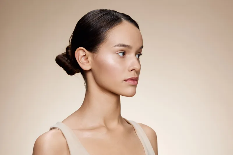 Elegant portrait of a young female model showcasing natural beauty with a soft expression against a creamy beige background, emphasizing skin care and minimalism