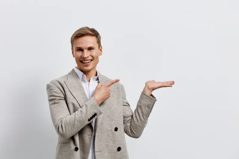 Smiling young caucasian man pointing hand digital nomad casual jacket white background studio portrait positive emotion
