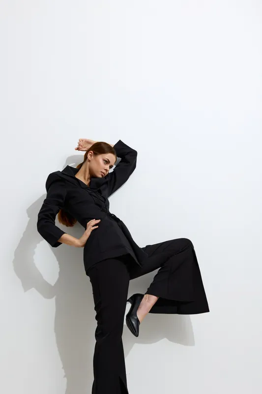 fashion woman in black stylish suit posing against white background with dramatic shadow, showcasing modern and minimalist aesthetic in high fashion photography.
