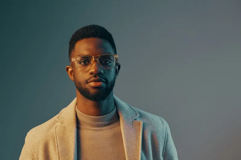Stylish young man in a light coat and glasses, displaying confidence and calmness against a gradient background, perfect for fashion or lifestyle concepts