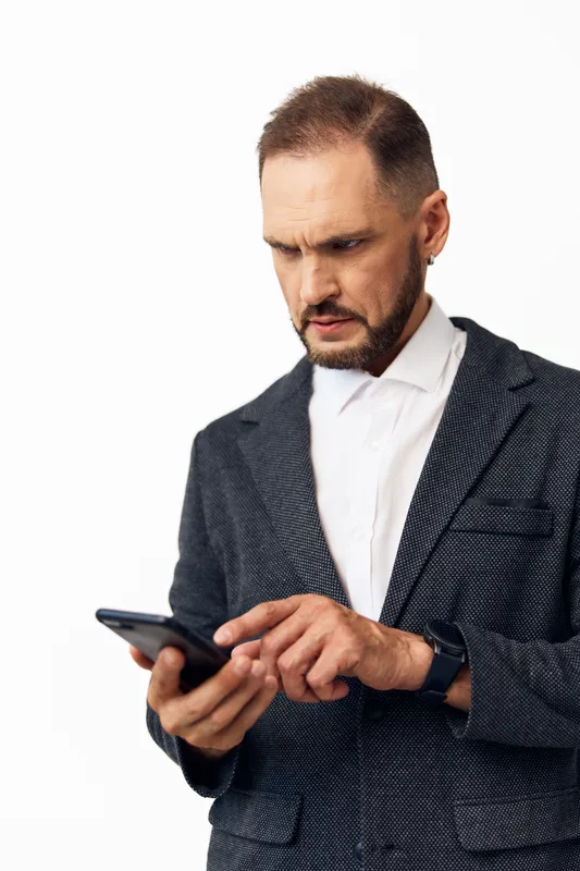Professional businessman on a neutral colored background, focused and thoughtful at work, expressing concentration and concern as he checks his device.