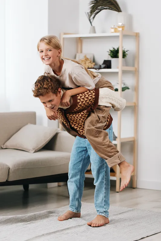 Joyful piggyback moment in a cozy living room, featuring a smiling child riding on a playful adult's back, capturing light, warmth, and carefree family happiness.