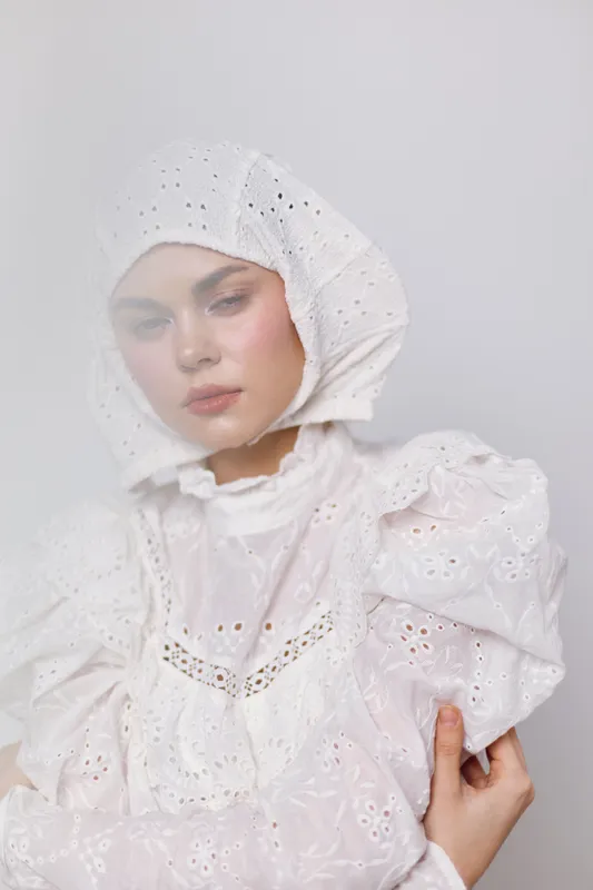Elegant female model wearing a delicate white dress and headscarf, showcasing a serene expression against a soft, minimalist background