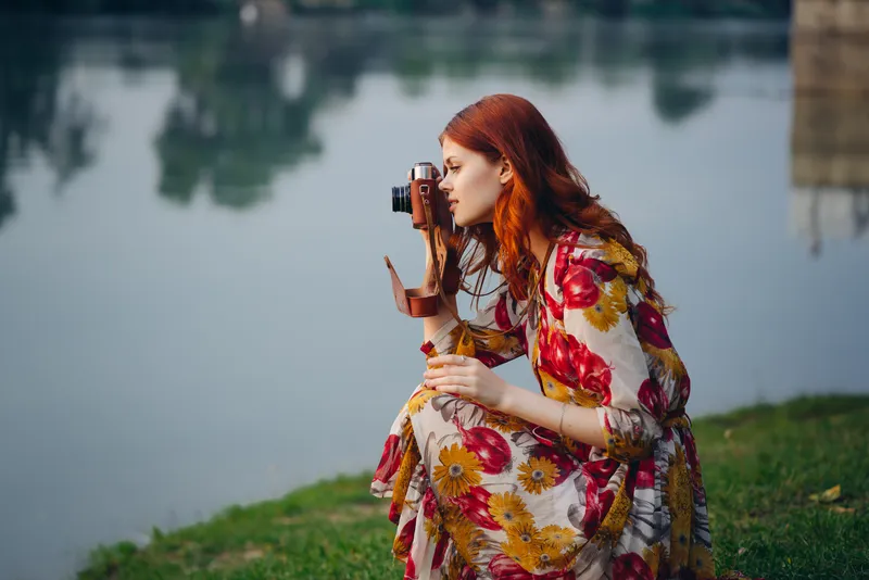 Рыжеволосая женщина с фотоаппаратом на природе у озера