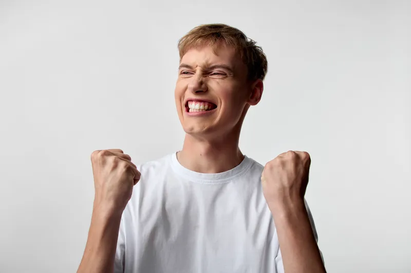 Energetic young man in a plain white t shirt clenches fists in triumph, conveying victory, celebration, excitement, motivation, energy, and a strong success mood for achievement campaigns.
