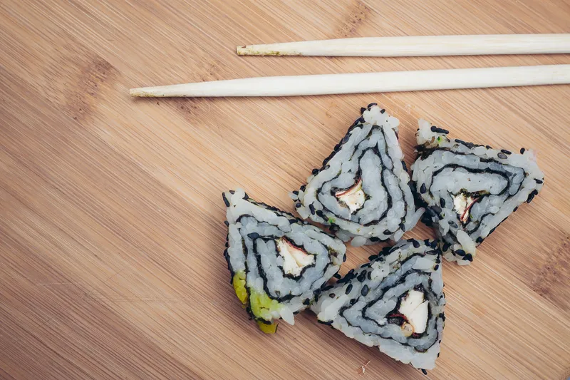 Треугольные роллы суши, палочки, деревянная доска, японская кухня
