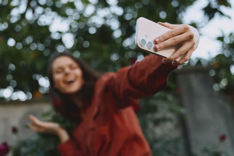 Smiling woman taking a selfie outdoors in a casual jacket. Natural background, lifestyle scene, well being, and self confidence. Soft light creates a warm, vibrant mood