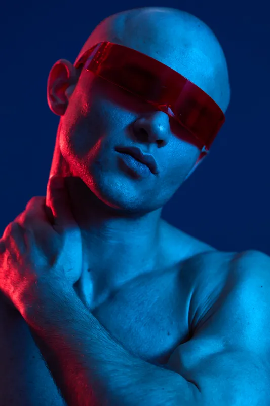A striking portrait of a man wearing bold red sunglasses, showcasing a unique color light effect with a blue background. This image captures modern style and attitude.