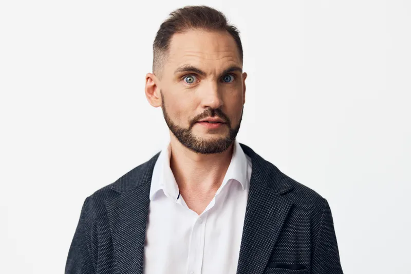 A business professional man stands against a bright colored background, exuding confidence and focus, portraying a poised, executive mood suitable for corporate portrait and marketing use.