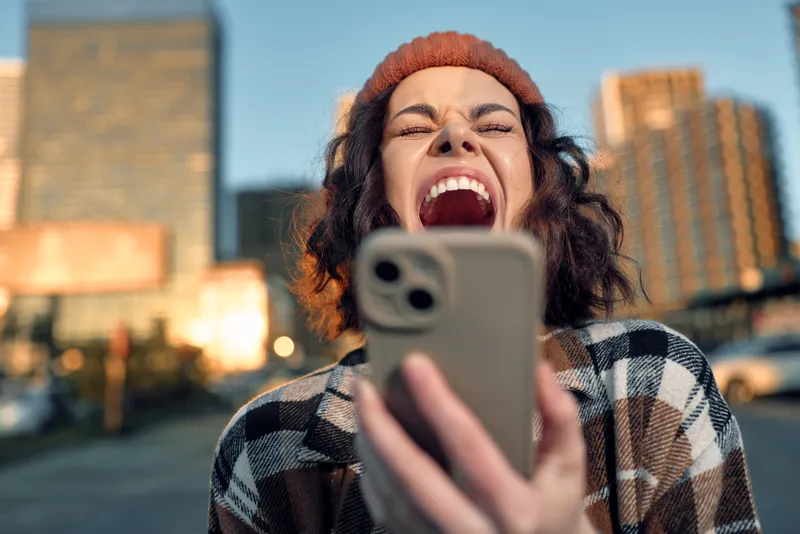 woman phone laugh city candid golden beanie joy. Authentic candid lifestyle portrait of a young woman shouting with phone at golden hour, emotional storytelling and mindful living vibe.