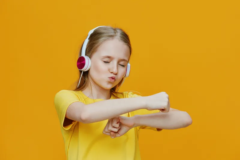 Joyful girl enjoying music, wearing headphones, dancing with vibrant yellow background, showcasing happiness and youthful energy in a bright summer scene