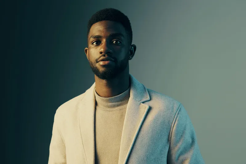 Stylish male model in a light coat and sweater, showcasing a confident expression against a gradient backdrop with a modern aesthetic, ideal for fashion concepts