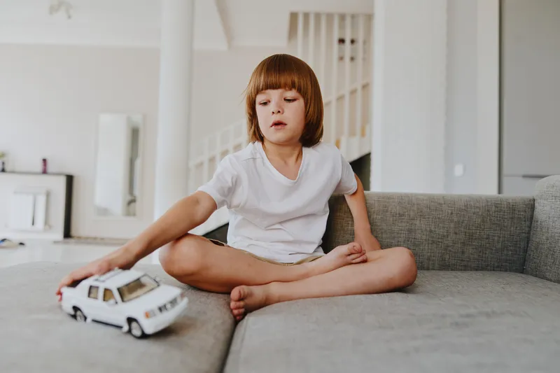 Young boy playing with a toy car in a bright living room, showcasing creativity and joy through playtime activities in a cozy home atmosphere.