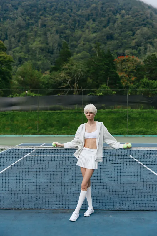 Young female tennis player in stylish tennis outfit on court, expressing confidence and focus against a lush green background with a modern sports vibe