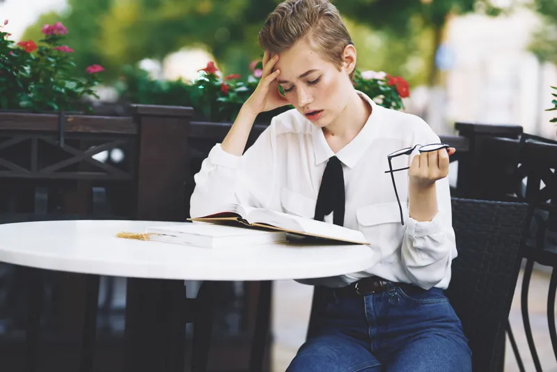 Студент с книгой в руках отдыхает на свежем воздухе, весело прогуливаясь по городу