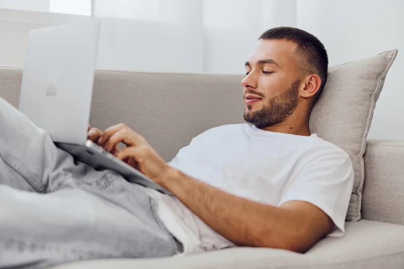 Relaxed man working on a laptop at home, showcasing modern lifestyle and remote work trends in a cozy living space with natural light.