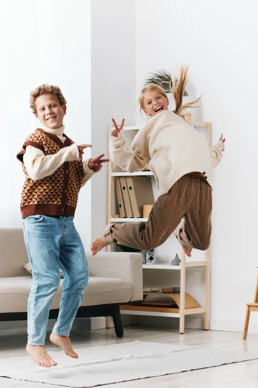 Authentic playful moment of children in a cozy living space, capturing dynamic movement and joy as they imitate school life and engage in spontaneous play.