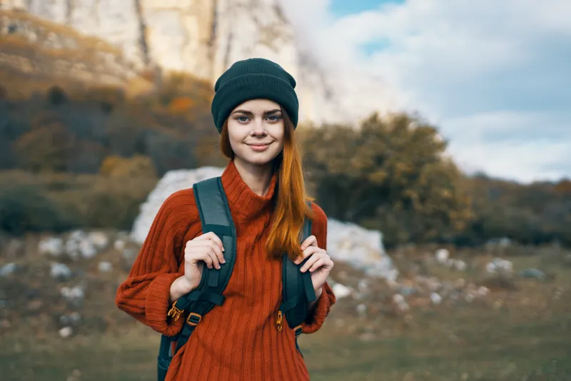 Симпатичная женщина-туристка в кепке на фоне горного пейзажа на открытом воздухе во время отпуска