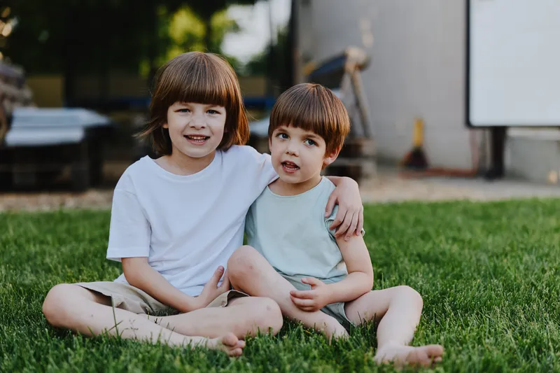 Two happy children sitting together outdoors in a sunny park, enjoying a playful moment on the grass, highlighting their friendship and joy.