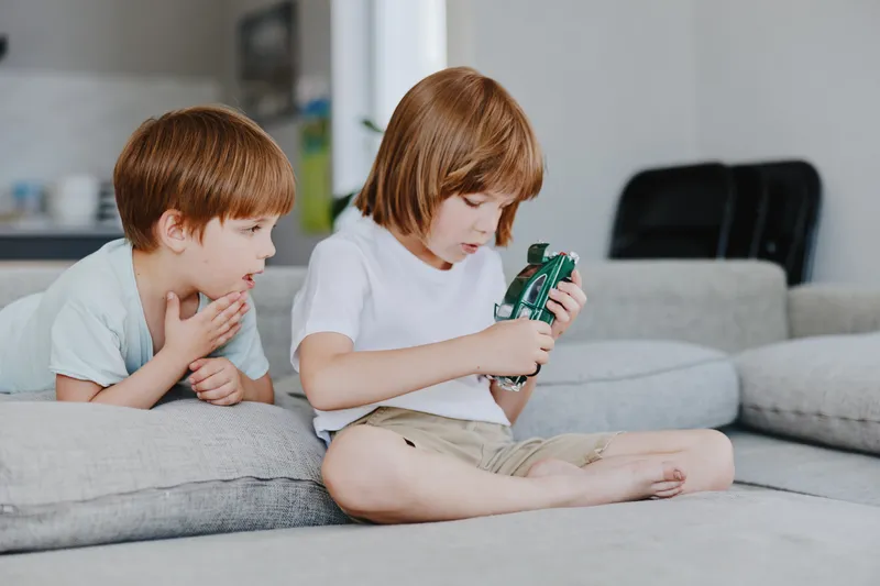 Two children engaging with a toy camera in a cozy living room, showcasing playful curiosity and innocence in their interaction.