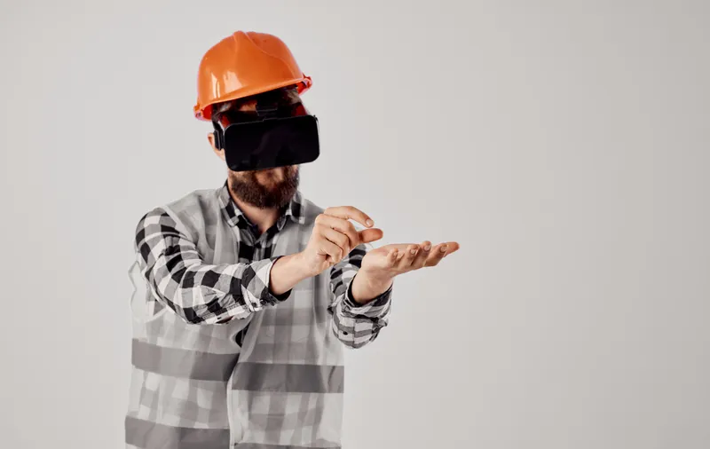 Архитектор в 3D-очках виртуальной реальности жестикулирует руками, на голове оранжевая каска