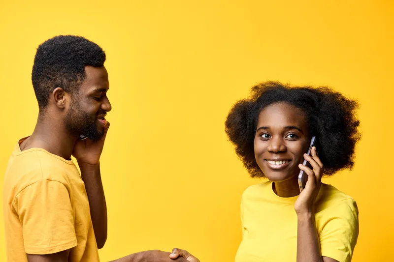 Two cheerful young adults interacting on mobile phones against a vibrant yellow background, showcasing a modern lifestyle and technology driven communication