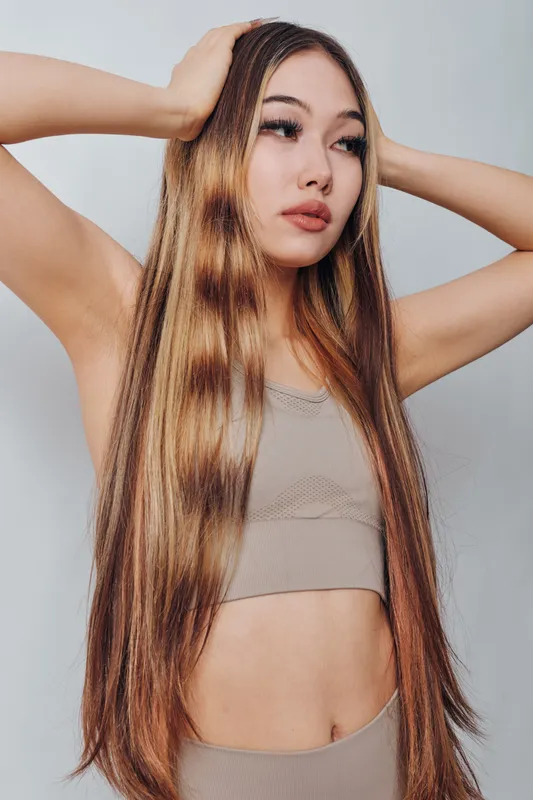 Young woman with long straight hair posing with hands on head in studio. Beauty, fashion, style, casual outfit, and natural makeup on female model.