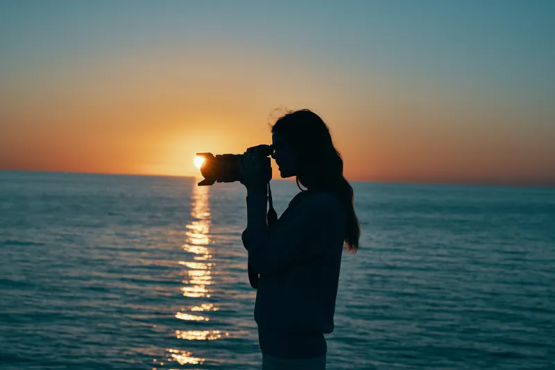 Женщина-фотограф с камерой на закате у моря, на пляже