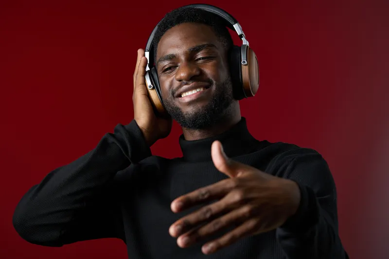 Young Black man enjoying music with headphones against a red background, showcasing joy and relaxation in a contemporary fashion style