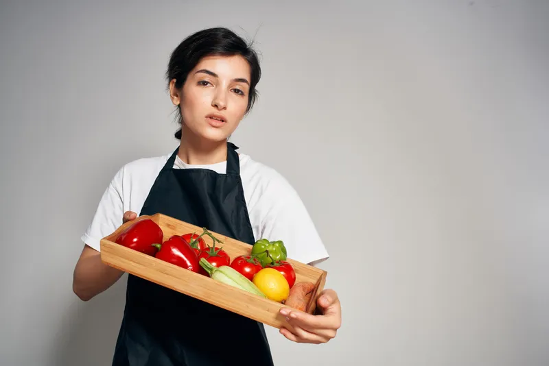 Женщина в черном фартуке держит поднос с овощами