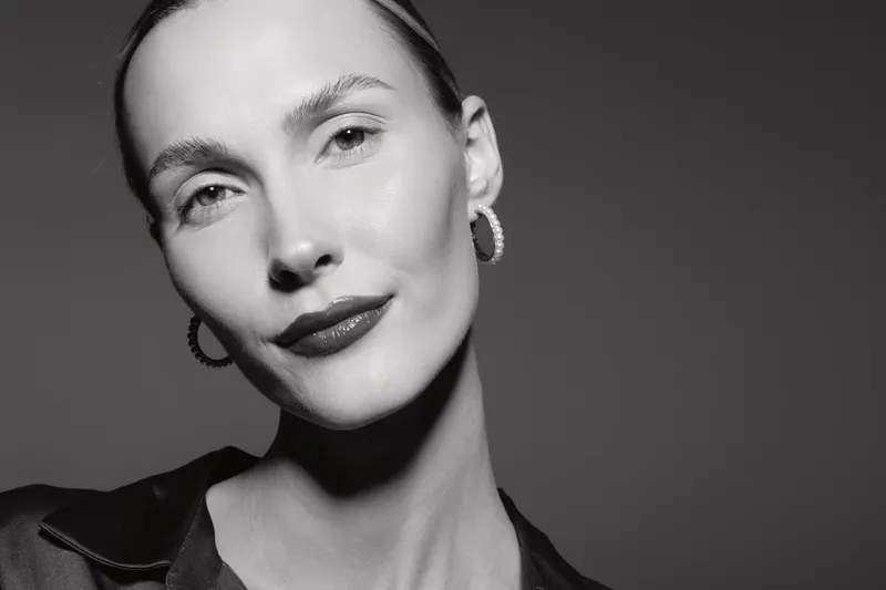 Closeup of a fair skinned Caucasian woman with slicked hair and earrings in black and white. Studio portrait with soft lighting highlighting facial features.