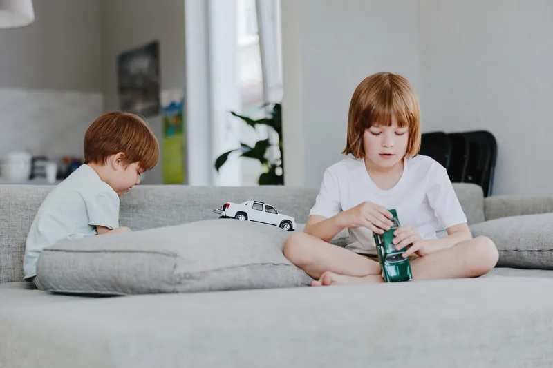 Two children playing with toy cars in a cozy living room, showcasing creativity and imagination. The scene captures a moment of joy and childhood innocence.
