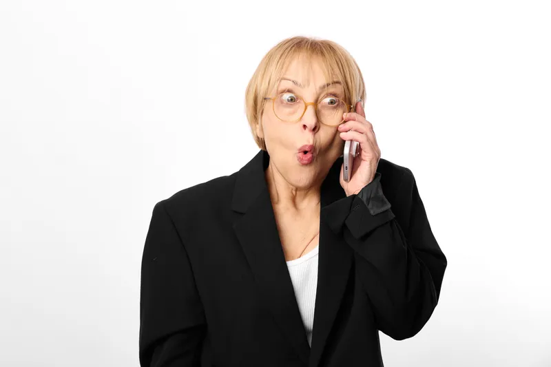 elderly woman in business suit answers phone with surprise and shock her face showing stress and anxiety during a work call isolated studio background concept of crisis