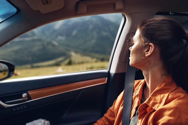 Driver in an orange shirt gazes through a car window at a rolling landscape, capturing a calm moment of travel and focus during a scenic road trip