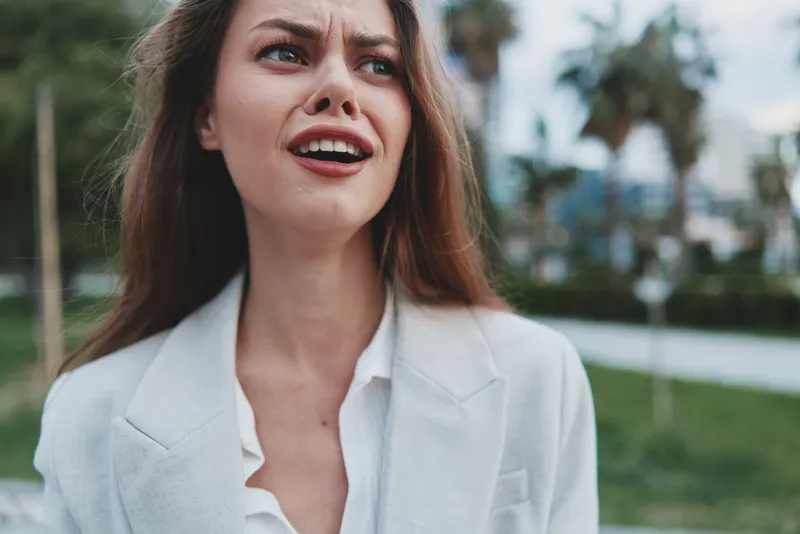frustrated woman in white blazer expresses stress and anxiety outdoor financial crisis concept with blurred city background
