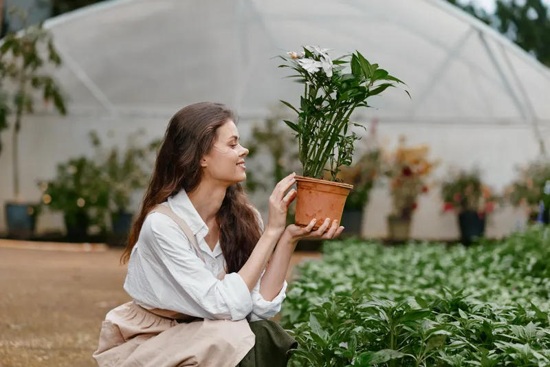 Young woman in a greenhouse holding a potted plant, symbolizing gardening joy and connection to nature, with lush greenery in the background