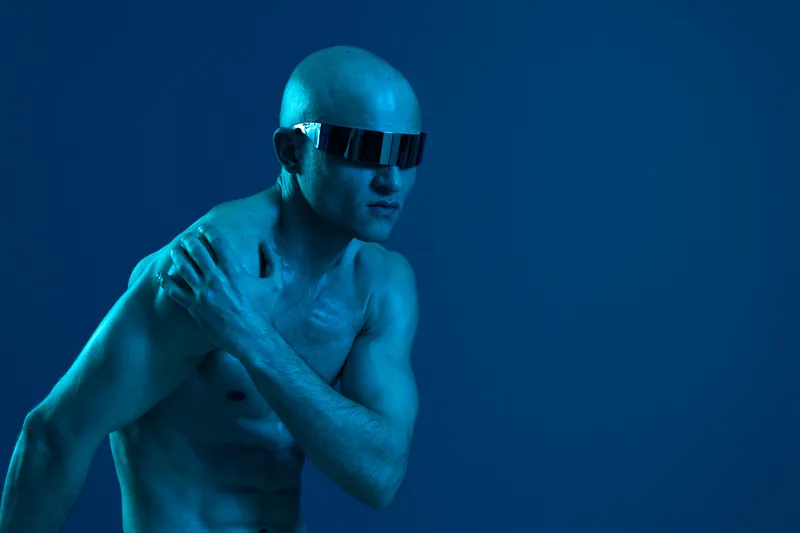 A striking image of a man with an athletic build, wearing sunglasses, showcasing a dramatic pose against a blue backdrop, evoking strength and style.