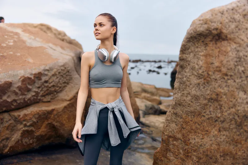 Fit young woman in sporty outfit standing by the seaside, confident and focused Athletic wear, headphones, natural background Inspirational fitness lifestyle