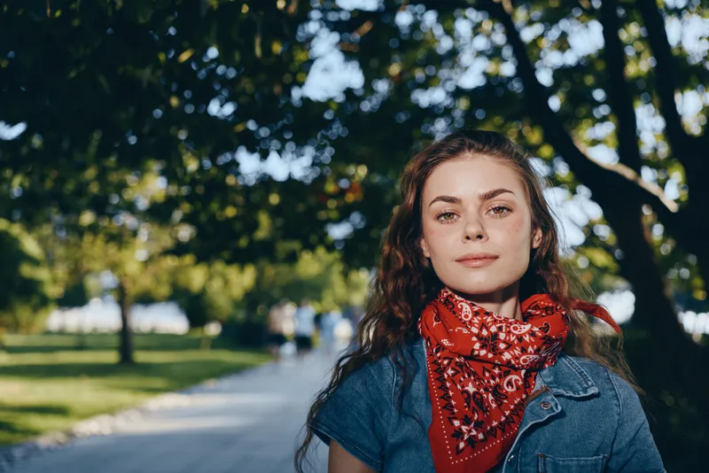 Lifestyle woman in modern boho-western denim street style with a red bandana, natural light, and film color effect creating a warm, casual outdoor atmosphere.