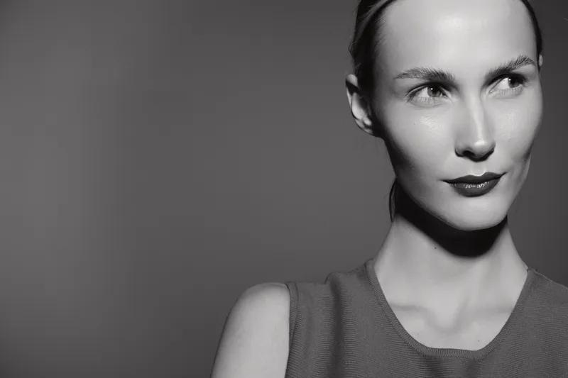 Young caucasian woman with fair skin looks sideways in black and white photo, minimalistic mood and soft lighting emphasizes facial features.