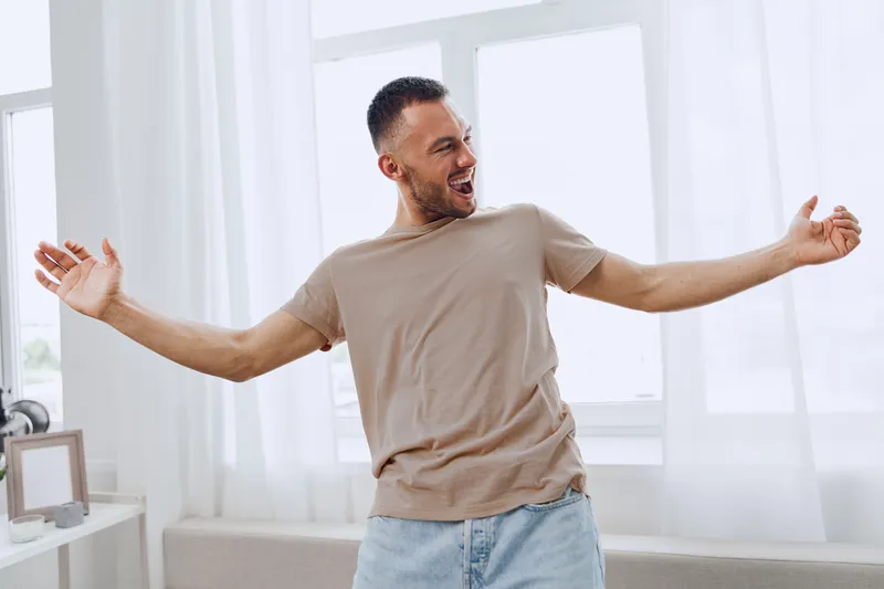 Happy man enjoying his free time, embracing moments of joy and authenticity in a bright, airy room filled with natural light.